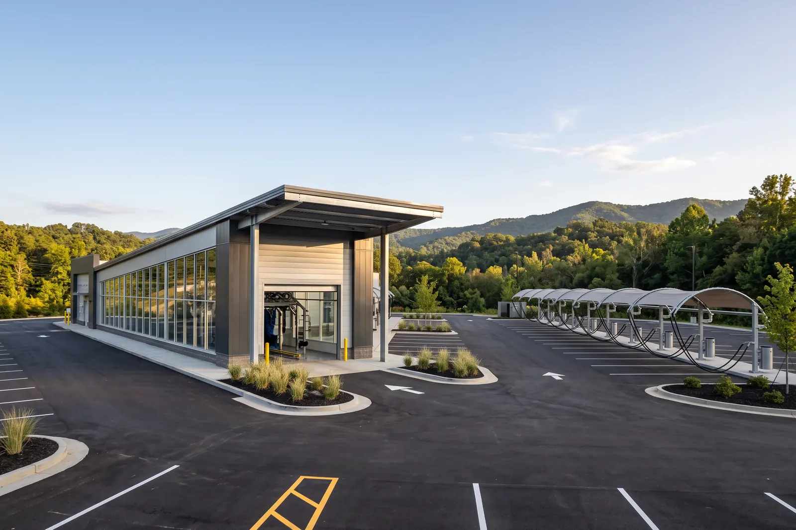 Illustrative image: a modern express tunnel car wash with a glass side wall and a row of covered vacuum stations, wooded hills behind.