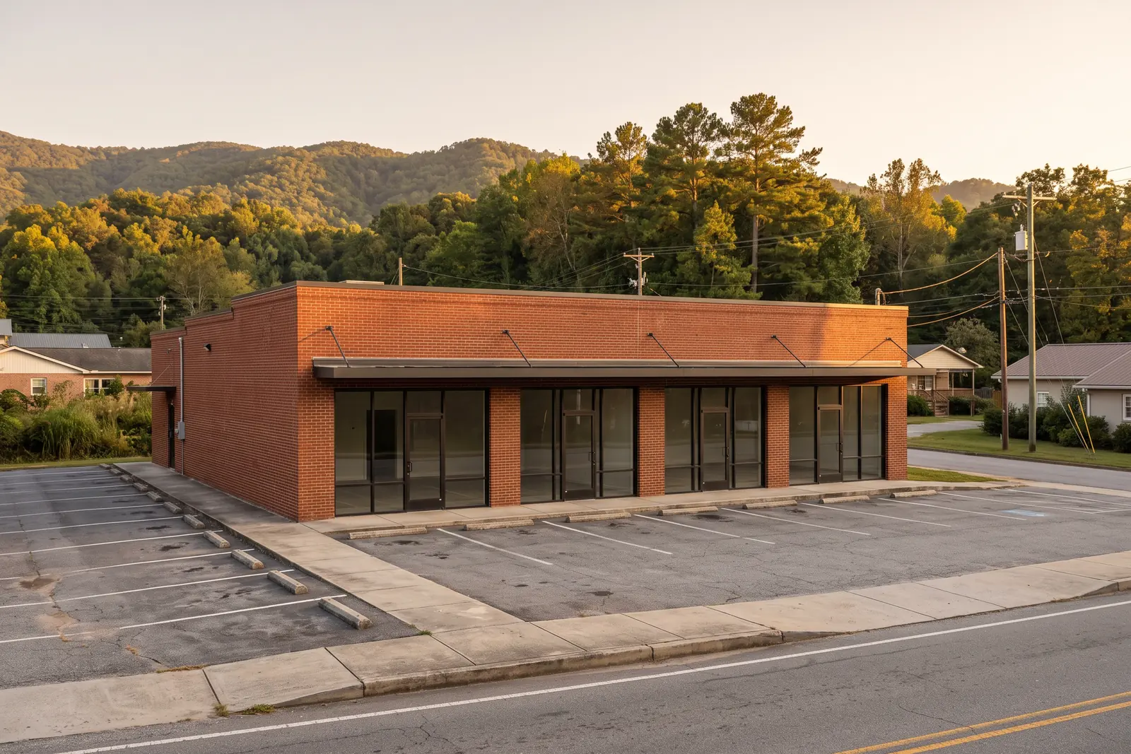 Illustrative image: a single-storey red brick retail building with dark storefront windows and an empty parking lot on a small-town street, wooded hills behind.