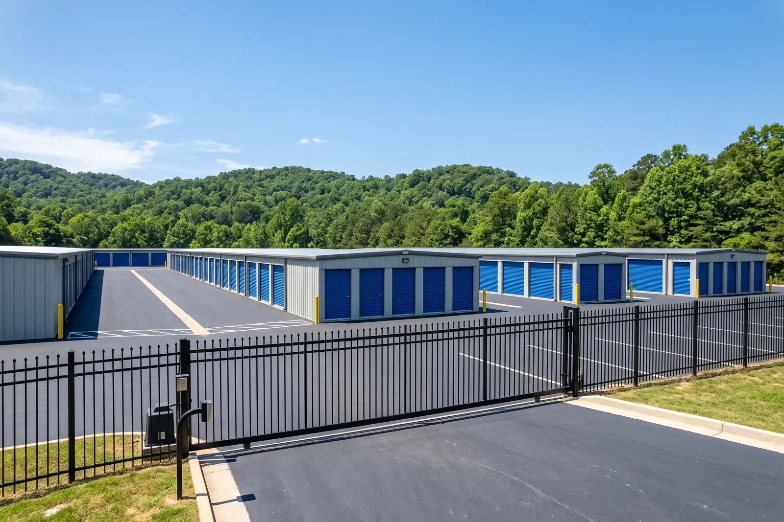 Illustrative image: a self storage facility with rows of blue roll-up doors behind a black security fence and gate, wooded hills behind.
