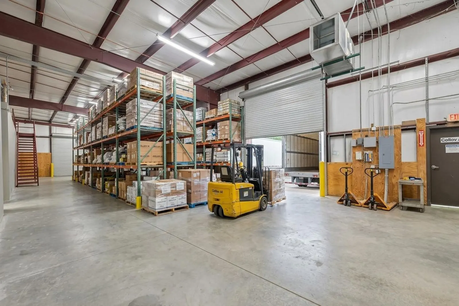 After: the same warehouse bay virtually staged with loaded pallet racking, a forklift and pallet jacks near the roll-up door.