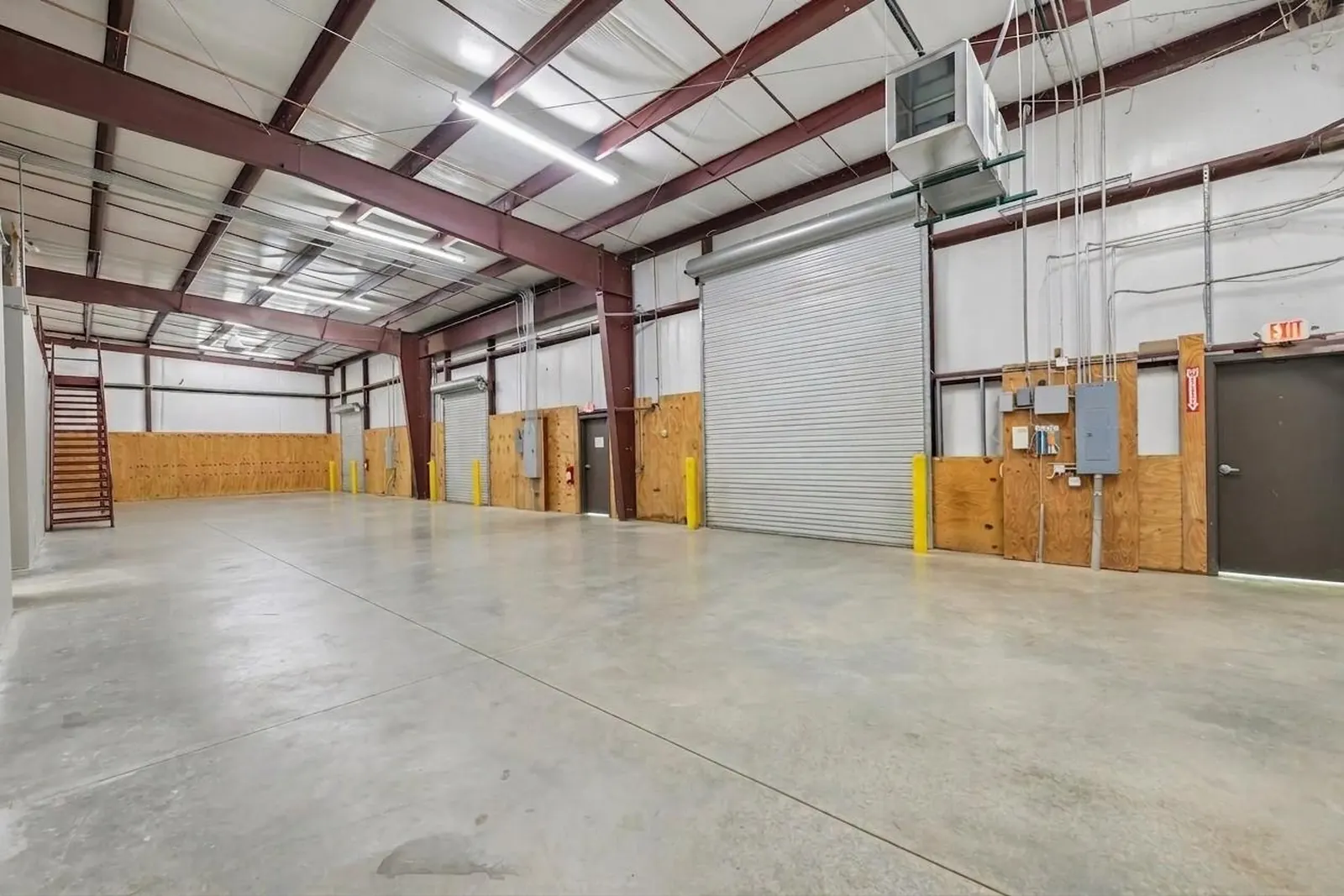 Before: an empty warehouse bay with a roll-up door, a plywood-lined wall with electrical panels and a stairway at left.