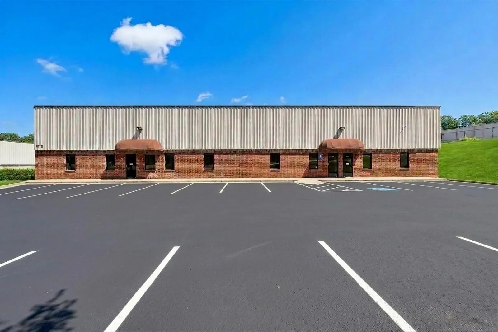 After: the same office-warehouse front across a freshly black parking lot with crisp white striping.