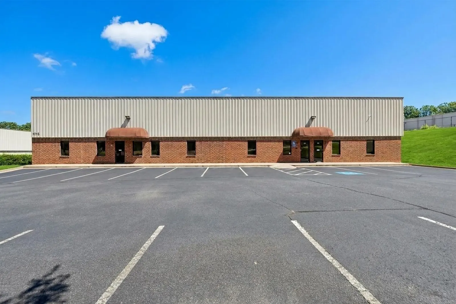 Before: the brick and metal front of a long office-warehouse building across a faded, cracked asphalt parking lot.