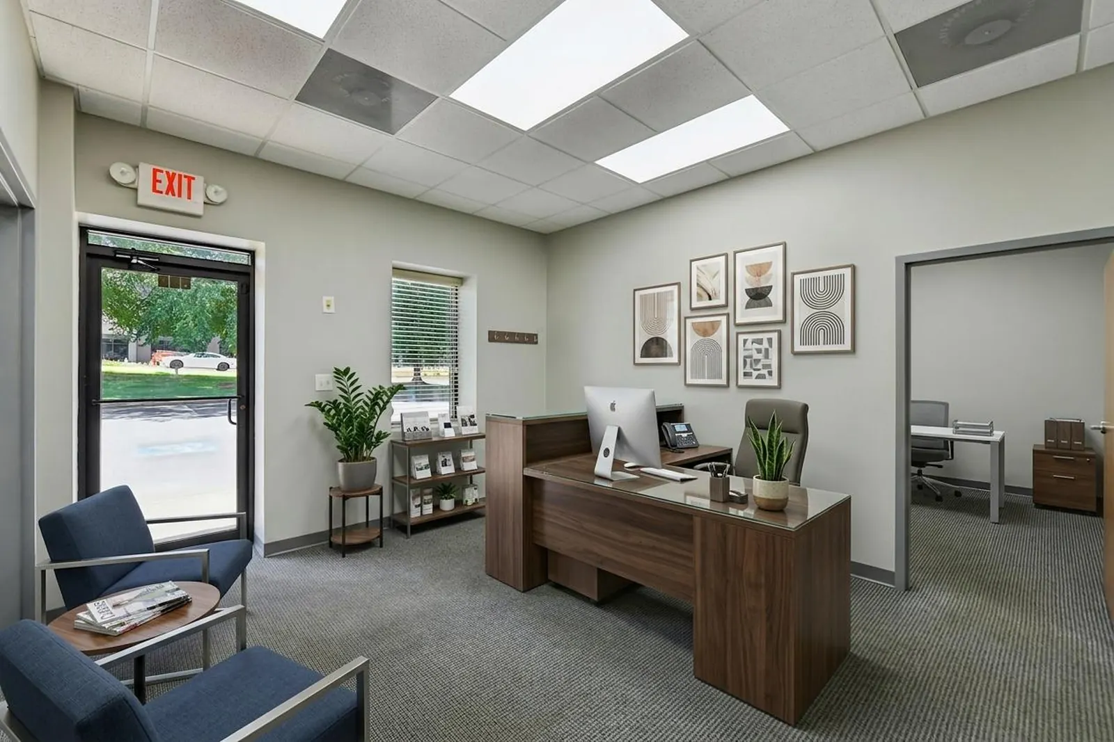 A virtually staged private office with a wood desk, a desk chair, a bookshelf, framed prints and a window.