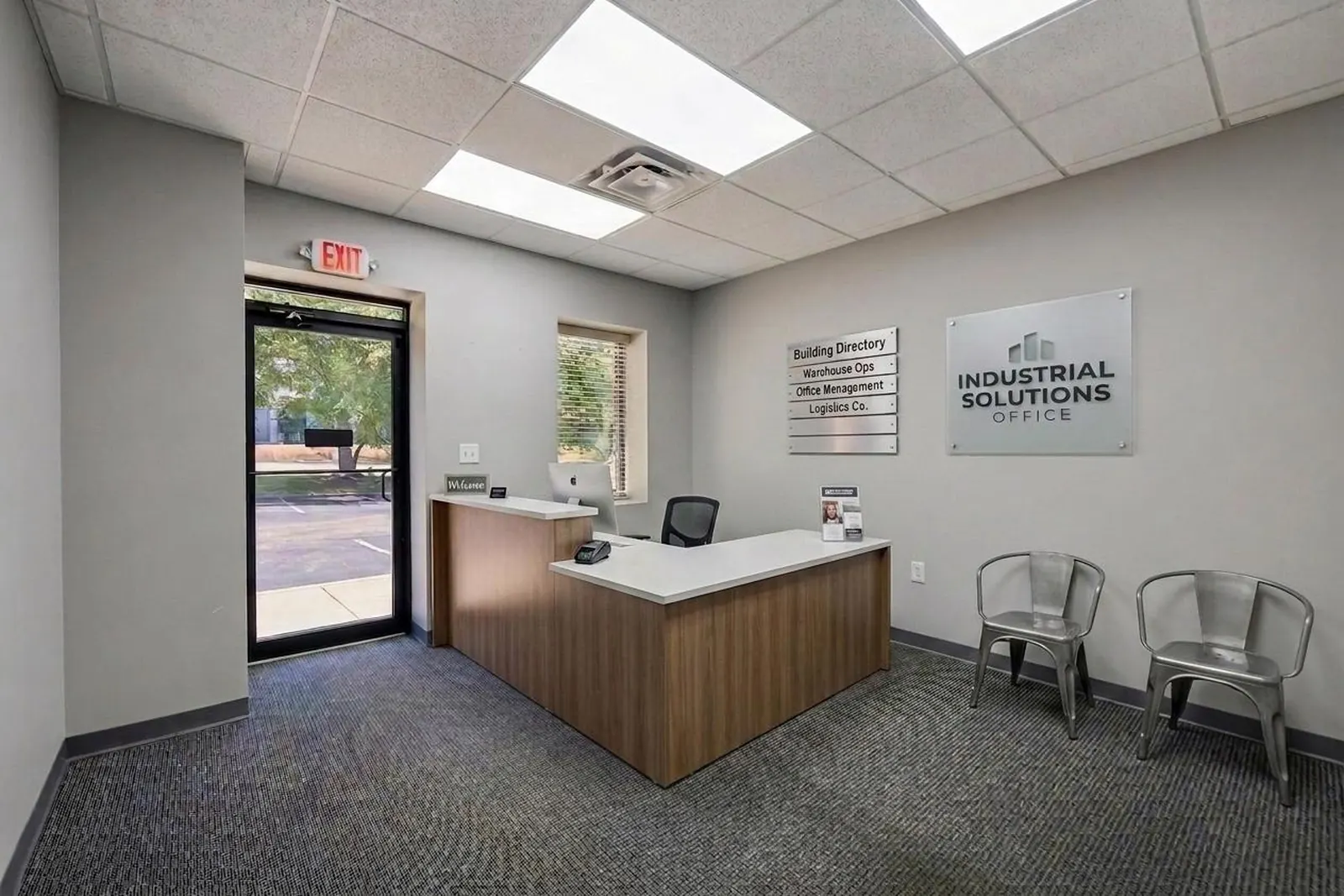 A virtually staged office reception area with a wood reception desk, two guest chairs, framed wall art and a glass entry door.