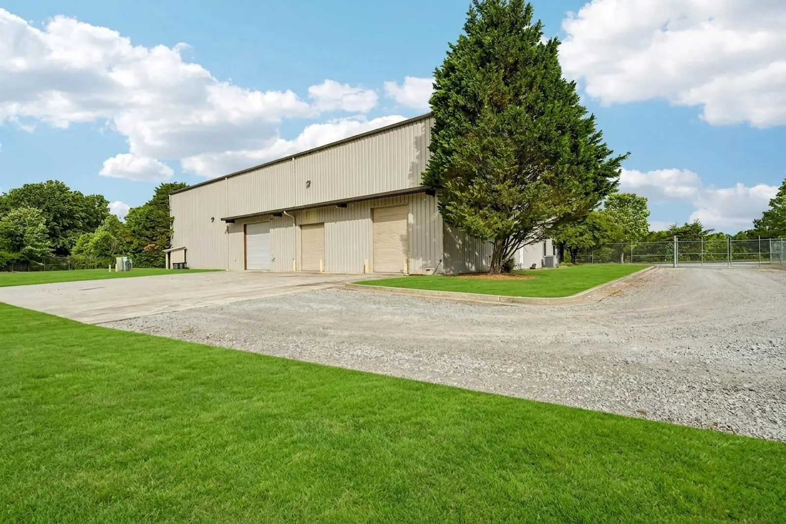 After: the same three-door side of the warehouse with the gravel apron intact and the weedy ground shown as green lawn.