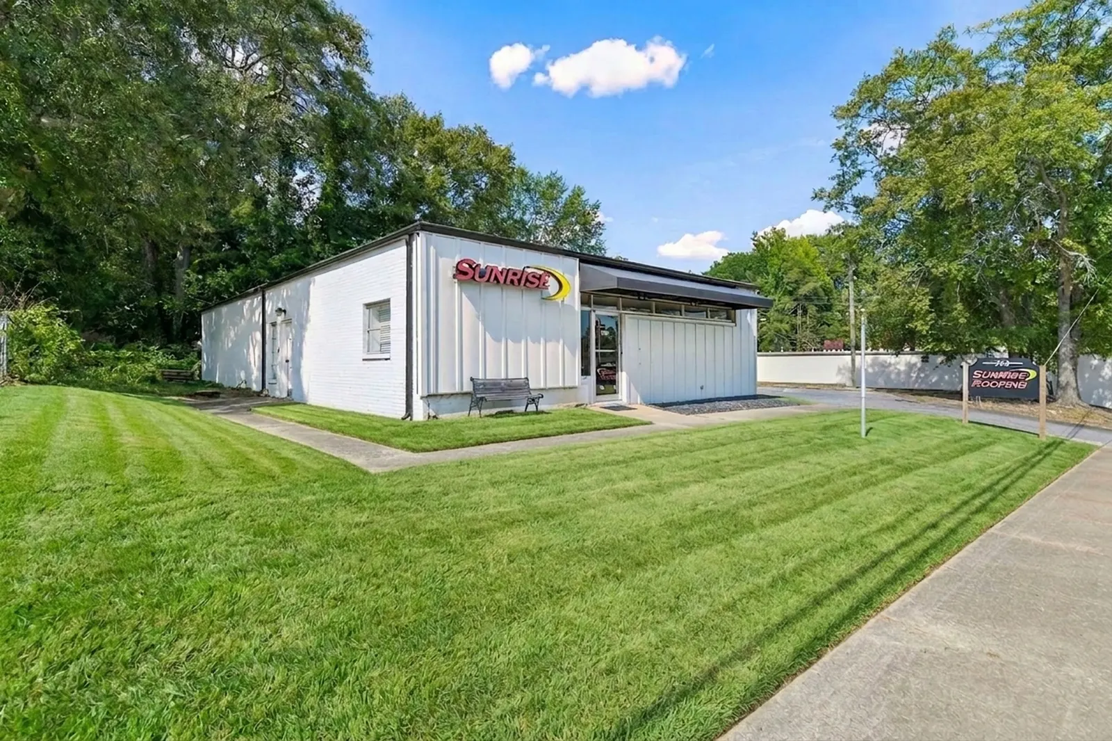 After: the same white commercial building across an even, striped green lawn.
