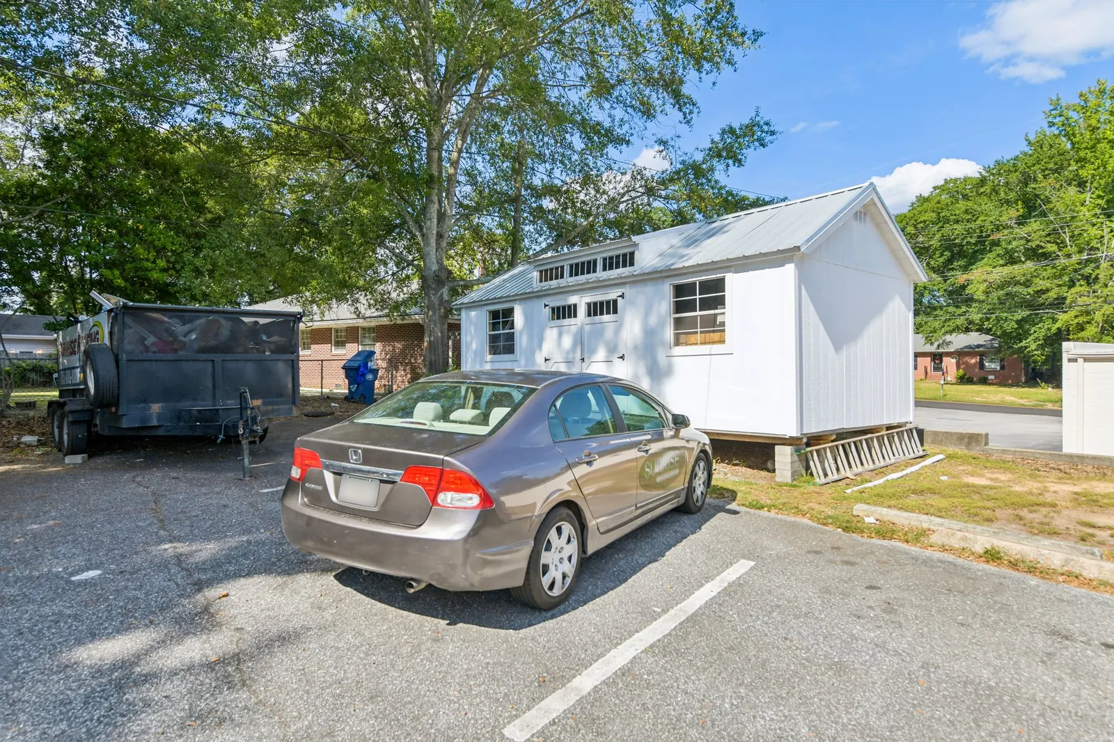Before: a rear parking lot with a parked sedan and a trailer in front of a white storage building.