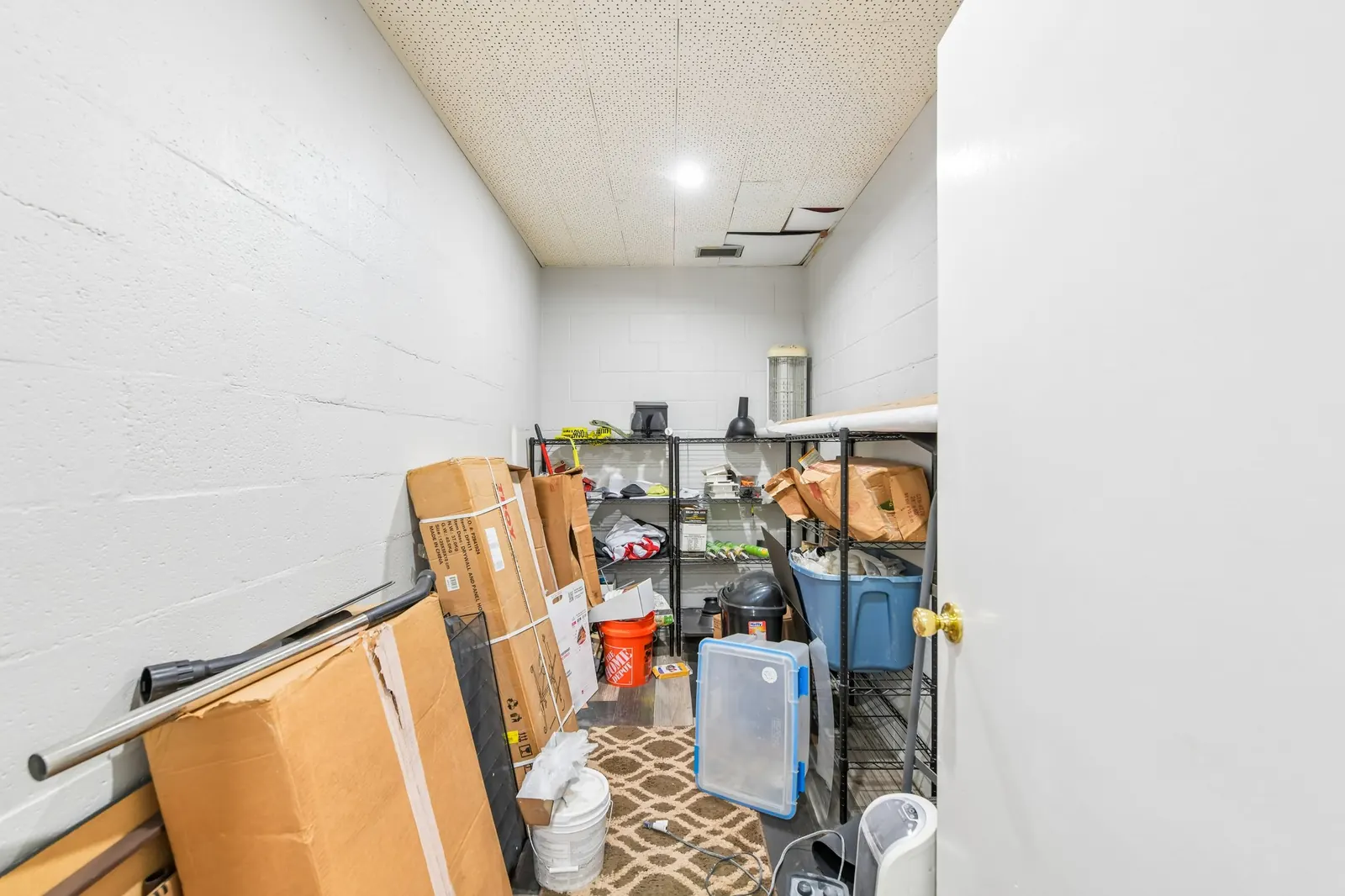 Before: a narrow storage room crowded with cardboard boxes, buckets, plastic bins and loose supplies in front of wire shelving.