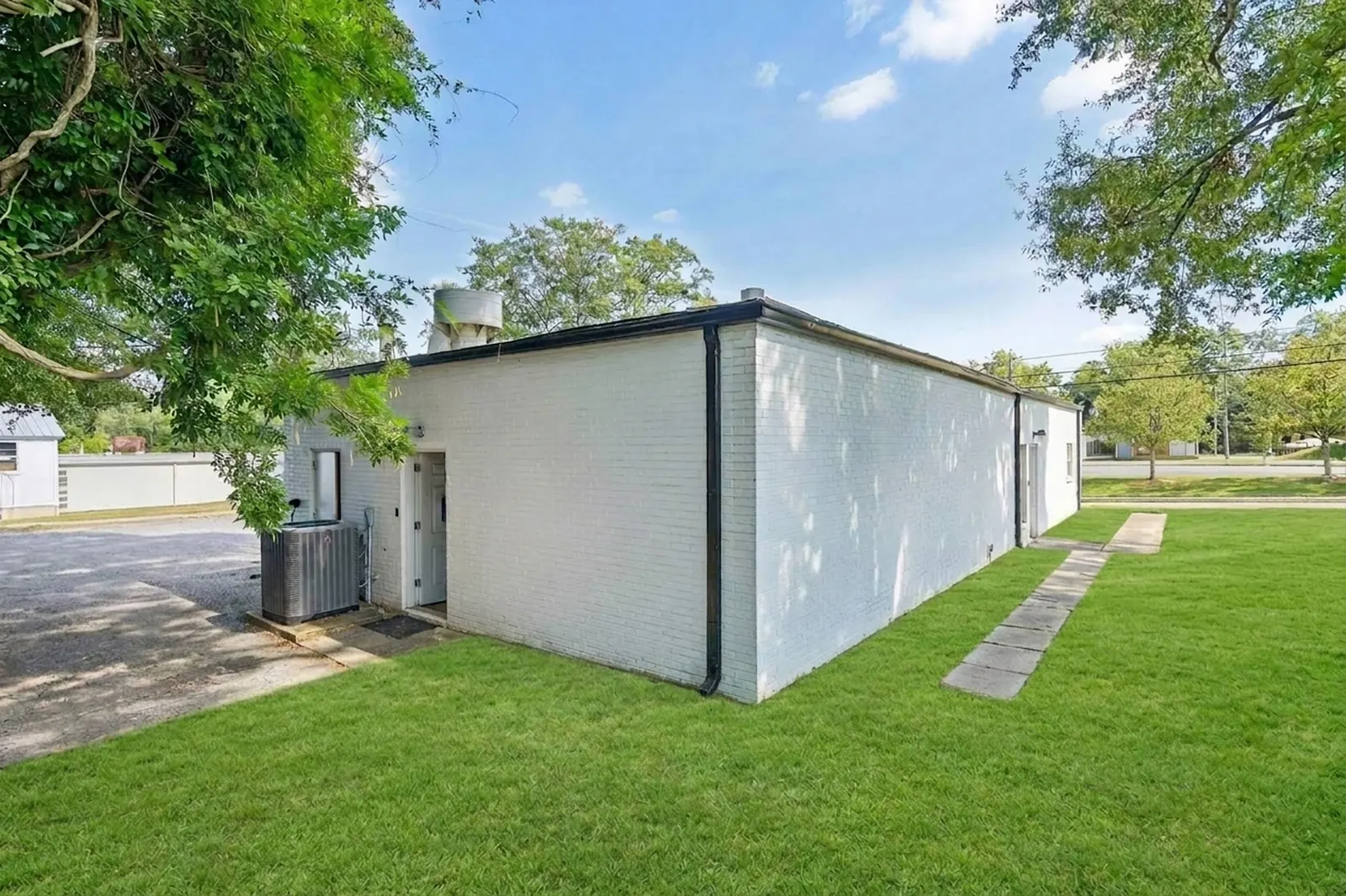 After: the same side of the white painted-brick building with the debris cleared and a green lawn along a paver walkway.